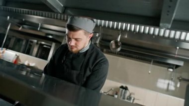 Otel şefinin restoranındaki profesyonel mutfak düşünceli bir şekilde duruyor ve aşağıya bakıyor.