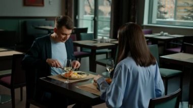 Otel restoranında randevuya çıkan erkek ve kadın beyaz şarap bardakları içer ve lezzetli yemekler yer.