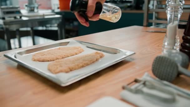 プロのキッチンで料理をするシェフがパン粉に油を盛ったチキンフィレを — ストック動画