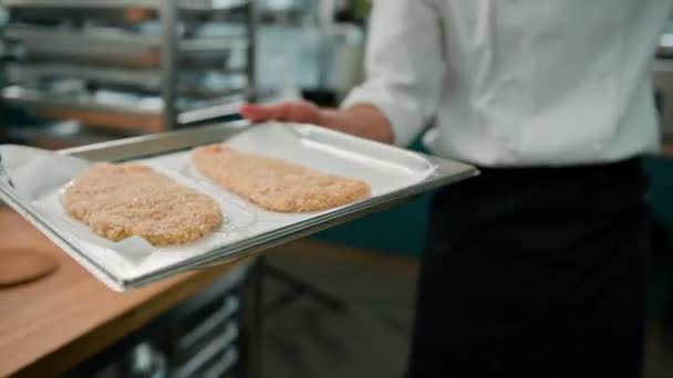 厨师在一个专业的厨房里放一张烤盘 上面夹着面包屑的鸡片放进烤箱 — 图库视频影像