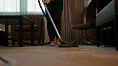 Üniformalı çalışkan bir hizmetçi otel odası konseptini temizlerken halıyı dikkatlice temizler.