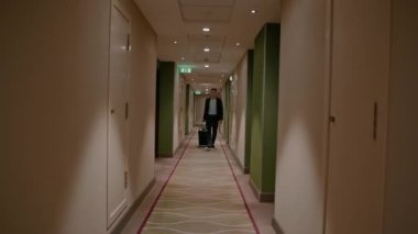 Bavullu bir adam otel koridorunda yürüyor. Seyahat gezisindeki iş adamının ön görüntüsü.