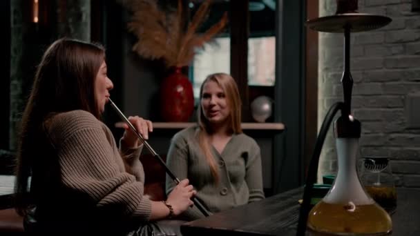 两个年轻的女性朋友正悠闲地坐在霍卡酒吧里 一边抽烟一边聊天娱乐 — 图库视频影像