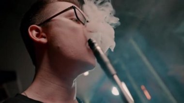 Bardaklı bir nargile adam geleneksel bir nargile piposu tüttürür. Bir adam nargile kafesinde ya da bar yakınlarında sigara tüttürür.