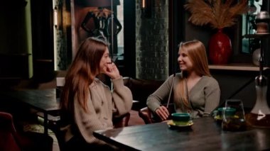 İki genç bayan arkadaş nargile barında rahatça oturup nargile tüttürüyor ve sohbet ederek eğleniyorlar.