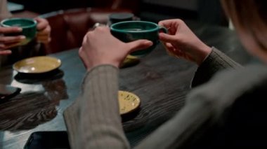 Genç kız arkadaşlar nargile odasında rahatça oturup bir şeyler tartışır ve çay fincanlarını masada içerler.