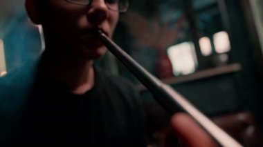 Bardaklı bir nargile adam geleneksel bir nargile piposu tüttürür. Bir adam nargile kafesinde ya da bar yakınlarında sigara tüttürür.