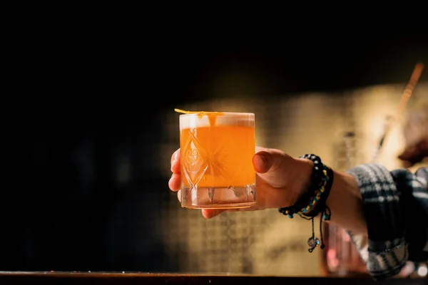 A close-up of a bar guest holding ready-made tasty peach sour alcoholic cocktail in his hand