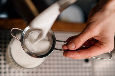 Barmen bitmiş kokteyli süzgeç alkolünden şeffaf bir bardağa doldurur.