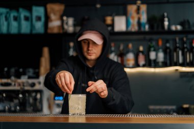 Barmen bardağa bir parça salatalık koyar. Barda salatalıkla birlikte alkollü bir kokteyl hazırlar.