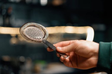 Barmenin kokteyl yapmak için kullandığı alet barın üzerinde süzgeç tutuyor.