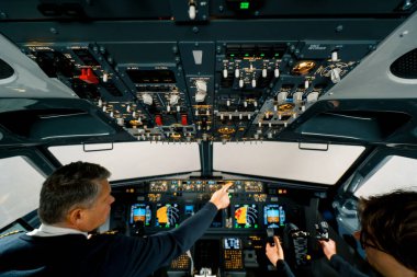 Deneyimli bir pilot, hava simülatörünün kokpitindeki eğitim uçuşundan önce genç bir öğrenciye talimat verir.