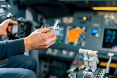 Tecrübeli bir pilot genç bir öğrenciye havacılık simülatörünün kokpitinde küçük bir model uçak gösterir.