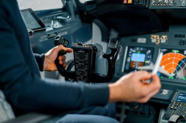 Tecrübeli bir pilot genç bir öğrenciye havacılık simülatörünün kokpitinde küçük bir model uçak gösterir.