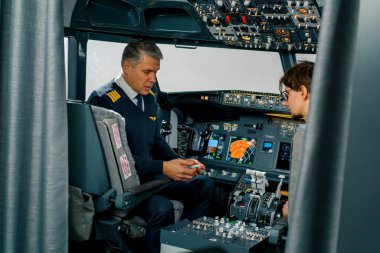 Tecrübeli bir pilot genç bir öğrenciye havacılık simülatörünün kokpitinde küçük bir model uçak gösterir.