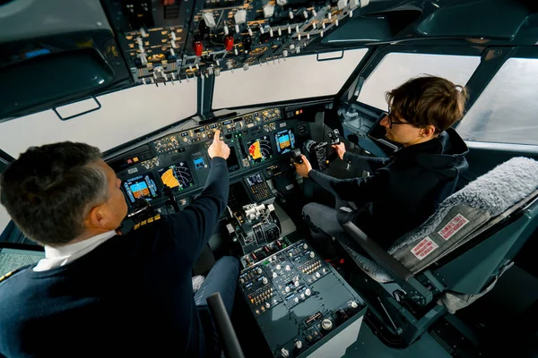 一名经验丰富的飞行员在飞行训练前在飞行模拟器驾驶舱给一名年轻学生授课 — 图库照片