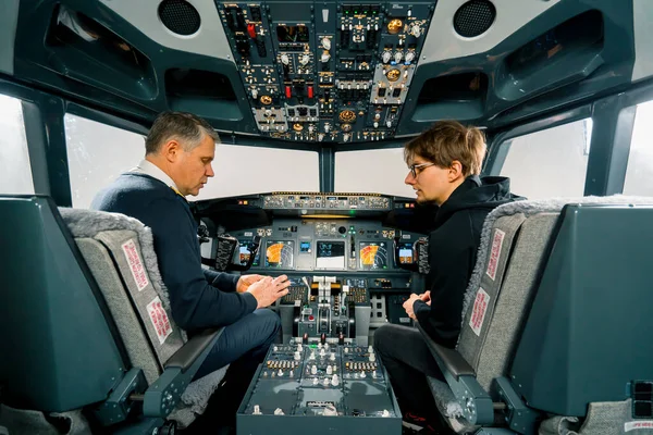 一位经验丰富的飞行员指导一位年轻的学生 并在飞行模拟器的驾驶舱里展示了一架小型模型飞机 — 图库照片