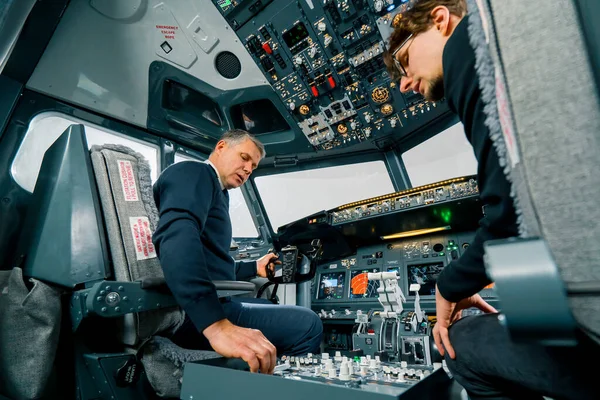 一名经验丰富的飞行员在飞行训练前在飞行模拟器驾驶舱给一名年轻学生授课 — 图库照片