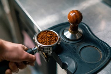 A professional barista in coffee shop prepares ground coffee by tamping fresh ground coffee beans close-up clipart