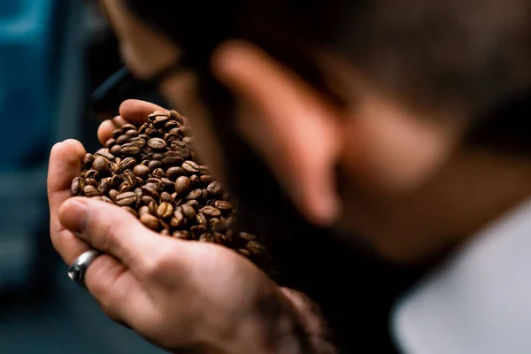 handsome worker sniffs coffee beans and checks the quality of coffee after roasting it in coffee factory machine