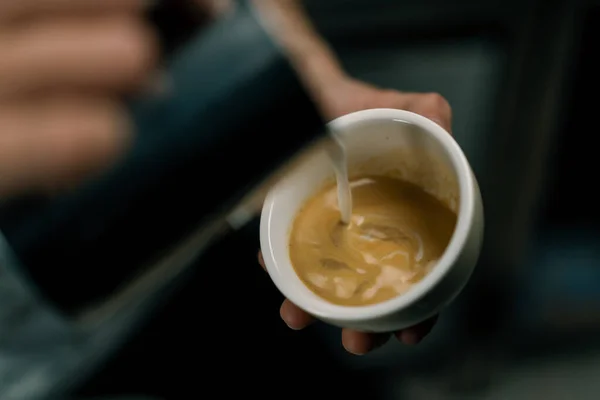 カフェでラテアートを作るバリスタ男性の手はパターンとカプチーノのカップにミルクの蒸気を注ぐ — ストック写真