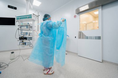 Hemşire ameliyat için hazırlanan ameliyathanede ameliyat üniforması giymeden önce cerrahın steril bir elbise giymesine yardım eder.