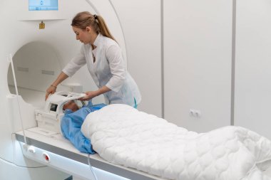 Tıbbi klinikteki bir radyolog cihazı hastanın kafasına, beyin manyetik rezonans görüntüleme prosedüründen önce yerleştiriyor.