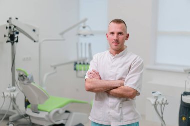 Ameliyata başlamadan önce dişçi muayenehanesinde duran yakışıklı genç bir dişçinin portresi.