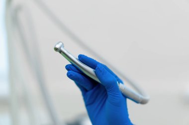 Profesyonel dişçi, klinikte işlem tamamlanmadan önce eldiven takılı diş türbini el çantasını tutuyor.