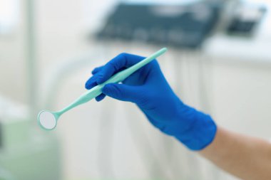 Profesyonel bir dişçi, klinikte işleme başlamadan önce eldiven içinde ayna tutar.