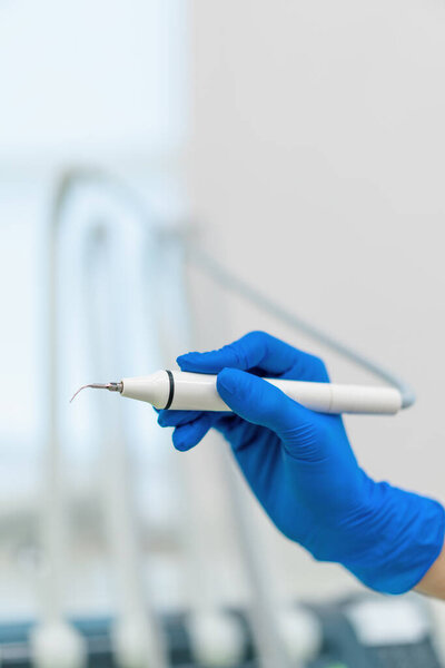 Professional dentist holding working tools for removing tartar in gloved hand before procedure in clinic close up