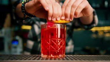 Barmen portakal kabuğunu sıkıyor ve negroni kokteylini süslüyor.