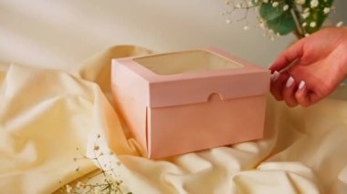 Lezzetli pastayı hediye kutusuna koydu. Bej arka plandaki adam kutuyu açtı ve tatlı tatlıyı gösterdi.