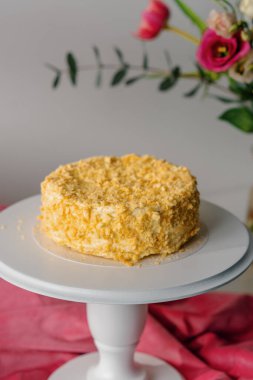 Çiçeklerin parlak arka planında beyaz bir standın üzerindeki puf böreğinden taze yapılmış Napolyon keki tatlı konsepti.