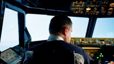 Modern bir yolcu uçağının pilotu kokpitten ön tarafa bakıyor.