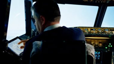 Pilot elinde bir tablet tutuyor, uçuş rotasına bakıyor ve uçağın iniş yerini seçiyor.