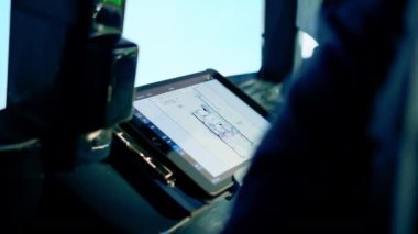 Pilot elinde bir tablet tutuyor, uçuş rotasına bakıyor ve uçağın iniş yerini seçiyor.