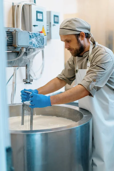 チーズ乳製品の生産で大きな鉄板とバチの柔らかいチーズの小さな部分を混合する労働者 — ストック写真