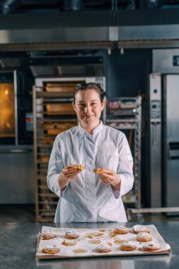 Güzel kadın fırıncı gözyaşları taze pişmiş sıcak aromalı çörekler hamur fırını üretimini kontrol eder.