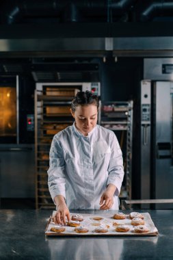 Güzel kadın fırıncı gözyaşları taze pişmiş sıcak aromalı çörekler hamur fırını üretimini kontrol eder.