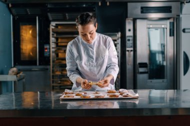 Güzel kadın fırıncı gözyaşları taze pişmiş sıcak aromalı çörekler hamur fırını üretimini kontrol eder.