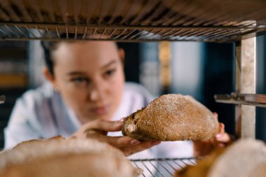 Raflar arasında çekici bir kadın fırıncı. Taze pişmiş ekmeğe bakıyor ve dikkatlice fırın endüstrisine bakıyor.