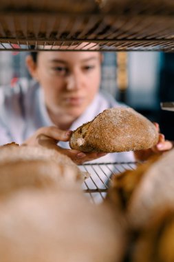 Raflar arasında çekici bir kadın fırıncı. Taze pişmiş ekmeğe bakıyor ve dikkatlice fırın endüstrisine bakıyor.