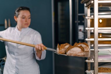 Kadın fırıncı fırından taze taze taze ekmek çıkarır ve fırın mutfağının mutfağındaki rafa koyar.