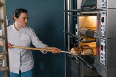Kadın fırıncı fırından taze taze taze ekmek çıkarır ve fırın mutfağının mutfağındaki rafa koyar.