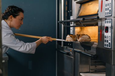 Kadın fırıncı fırından taze taze taze ekmek çıkarır ve fırın mutfağının mutfağındaki rafa koyar.