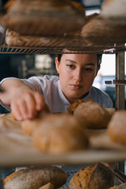Raflar arasında çekici bir kadın fırıncı. Taze pişmiş ekmeğe bakıyor ve dikkatlice fırın endüstrisine bakıyor.