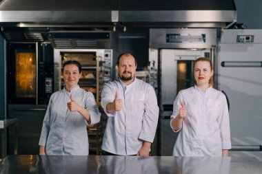 Pişirmeye başlamadan önce profesyonel bir mutfakta gülümseyen profesyonel fırıncılardan oluşan bir ekip.