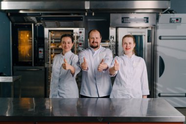 Pişirmeye başlamadan önce profesyonel bir mutfakta gülümseyen profesyonel fırıncılardan oluşan bir ekip.