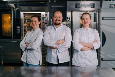 Pişirmeye başlamadan önce profesyonel bir mutfakta gülümseyen profesyonel fırıncılardan oluşan bir ekip.
